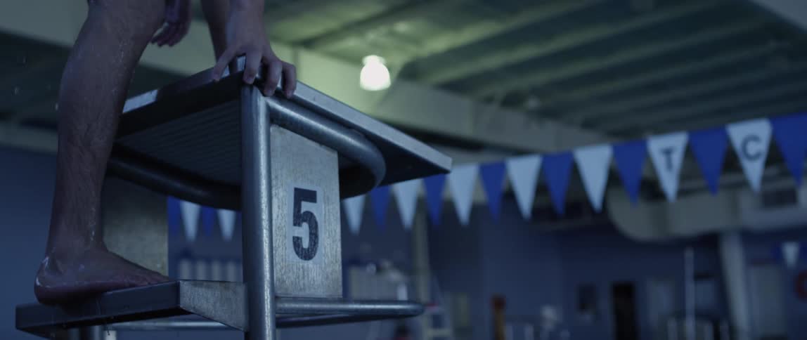 A man climbs atop a diving platform in an indoor pool