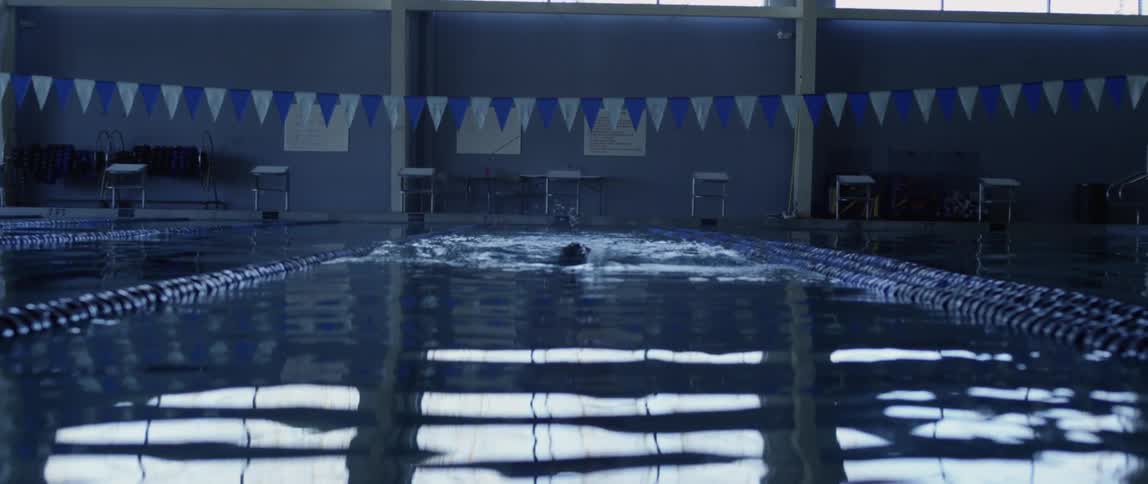 A man swims freestyle down the lane of an indoor swimming pool