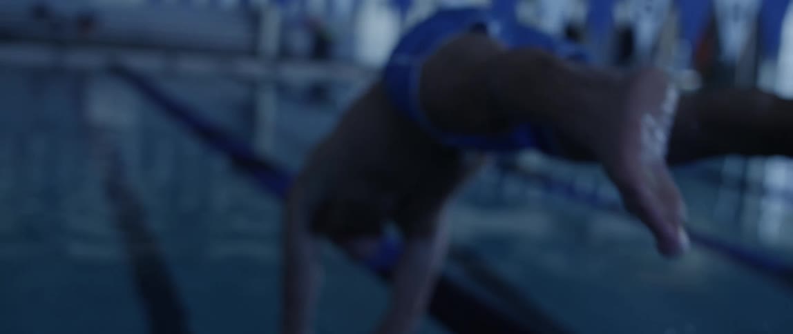 A man dives into an indoor swimming pool wearing blue swim trunks