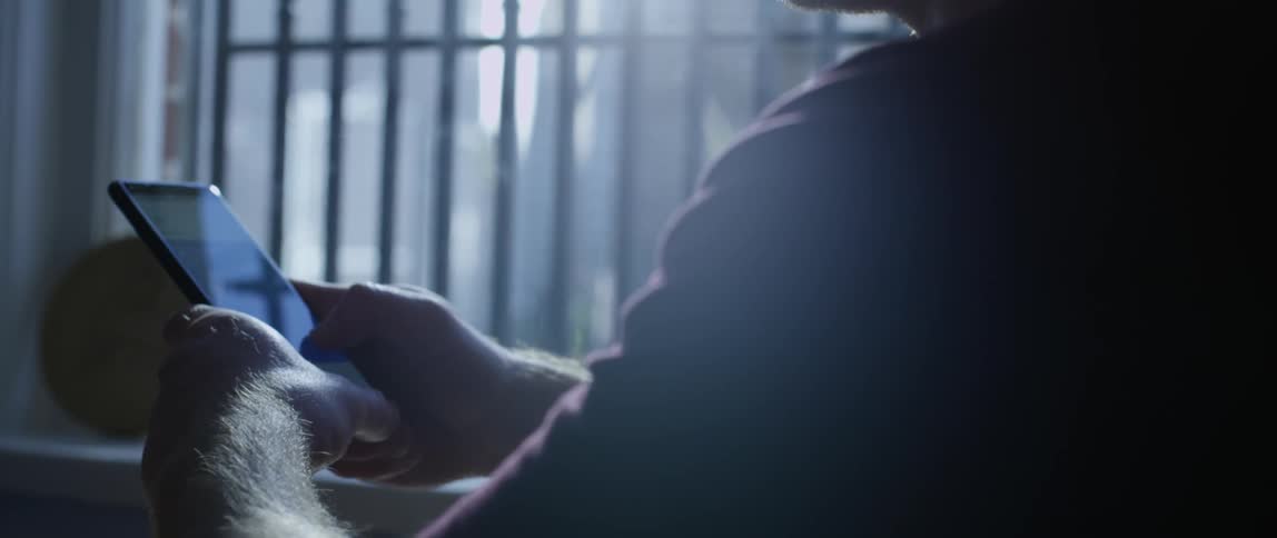 Man with his hands on a table indoors scrolling through a smartphone