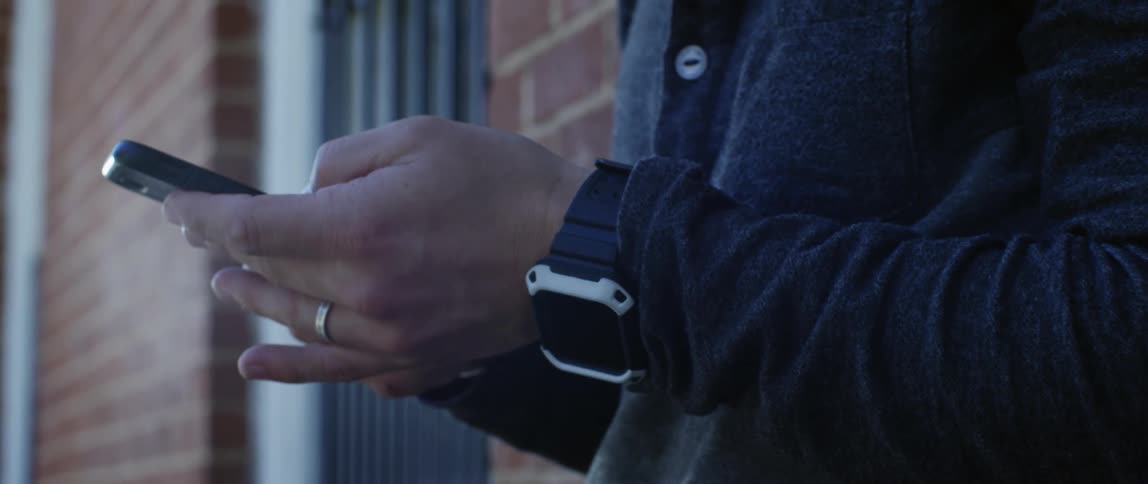 Man leaned against a brick building scrolling through a smart phone