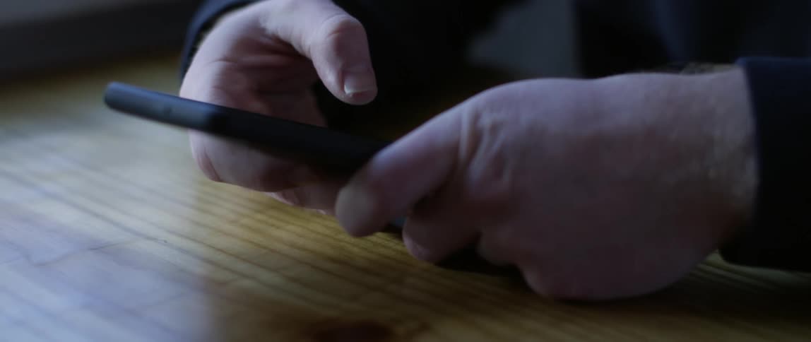 Hands scrolling through a screen on a smart phone at a wooden table