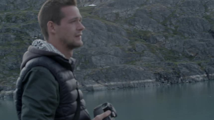 A man is photographing a lake with a mountain around him