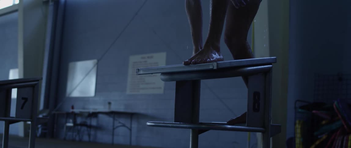 A competitive swimmer climbs up a small diving stand as water drips down his legs