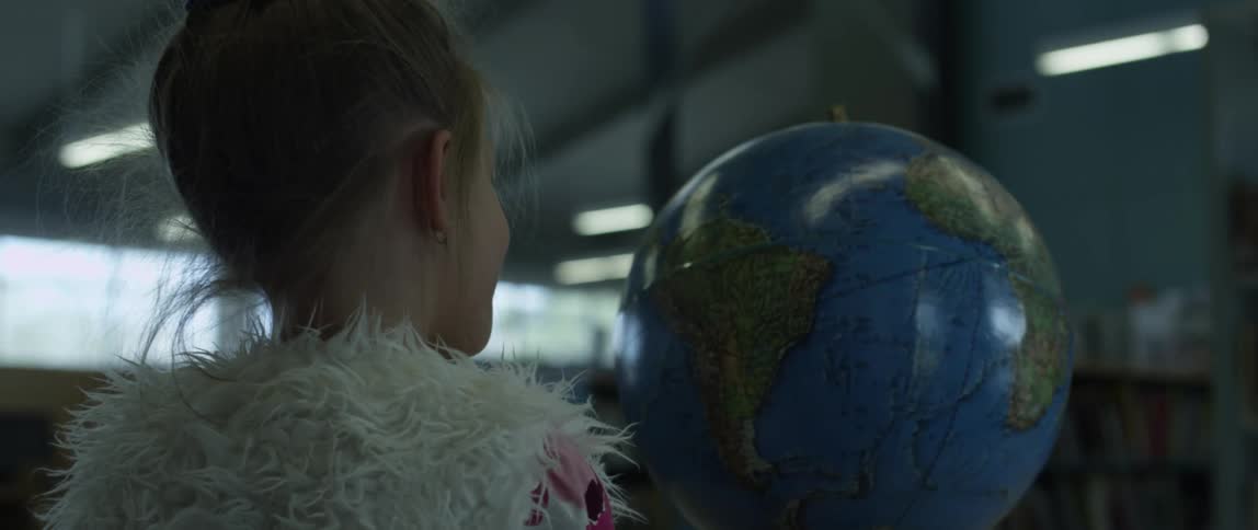 Girl looking at an earth globe spinning on a thread in a dimly lit warehouse