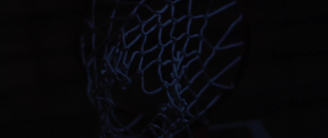 In the darkness a basketball is shot and swishes through a basketball hoop