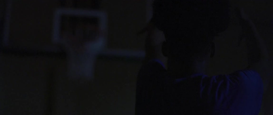 A man shoots a basketball in darkness