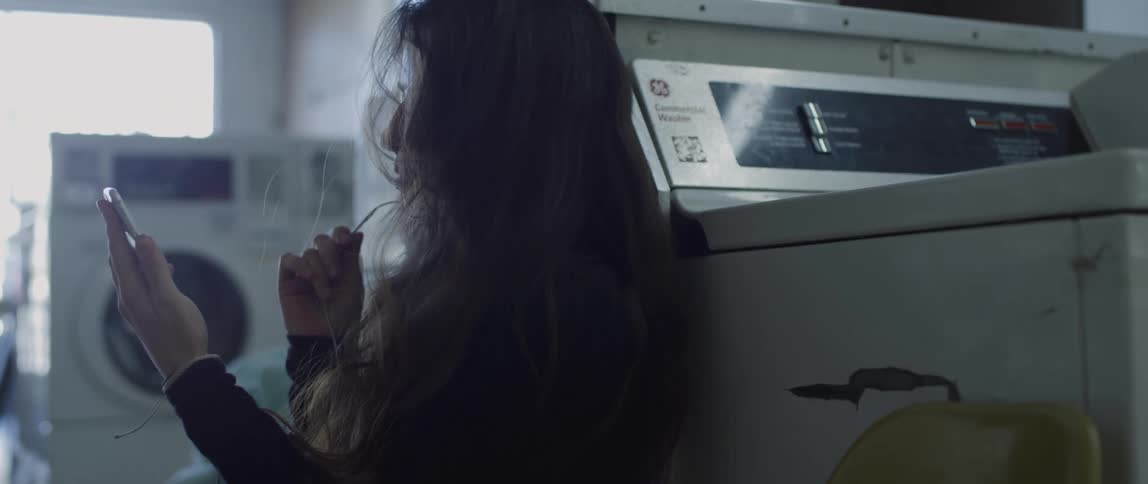 Woman sitting in a laundromat talks on her smartphone through the microphone on the earplugs