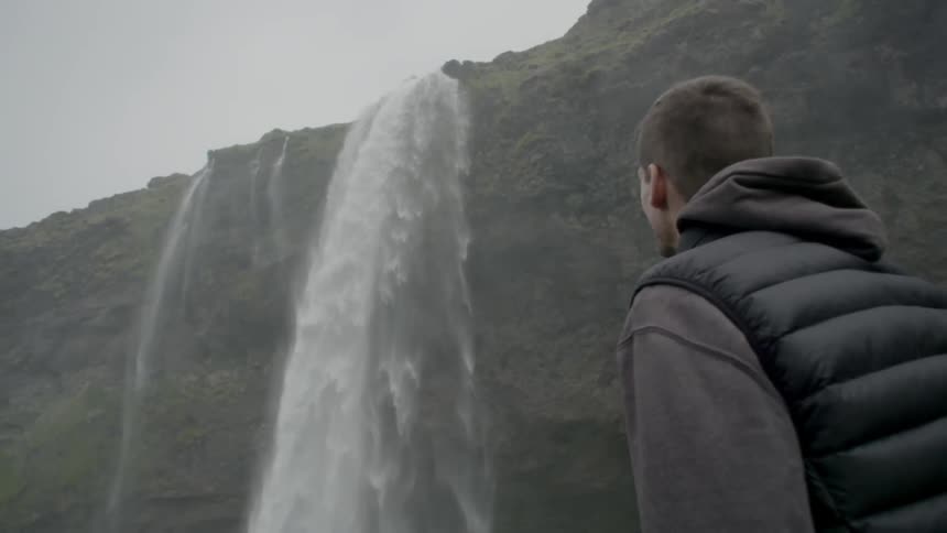 Man looking at a tall waterfall