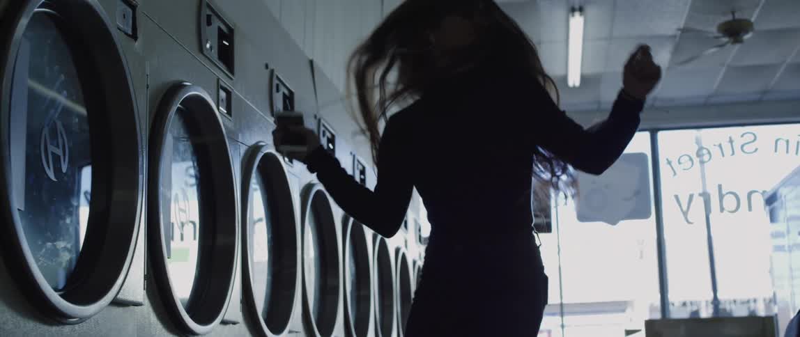 Silhouette of a long haired woman dancing to the music on her phone in a laundromat