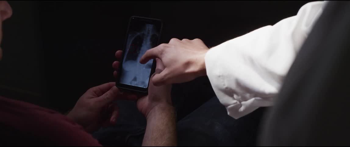 A doctor is with a patient pointing at a phone explaining an xray