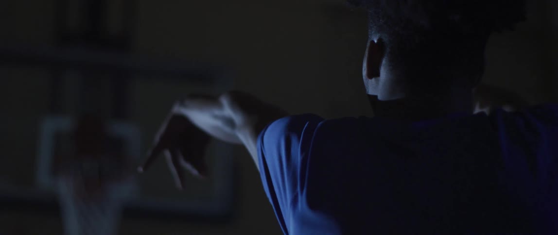Basketball player throws a basketball into a hoop on a dark court