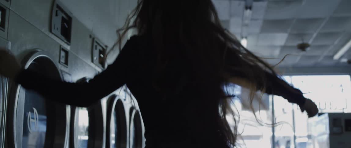 Silhouette of a woman dancing to the music on her smartphone in a dimly lit laundromat