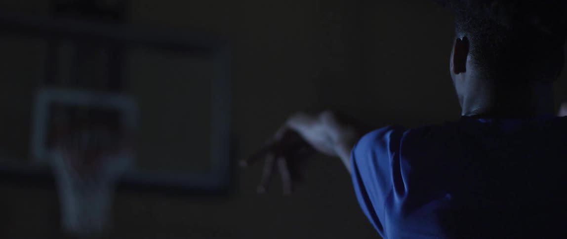 Man swishes a basketball into the hoop from a free throw line in a dark place