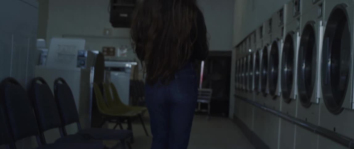 Woman walking in a laundry mat next to washing machines and dryers