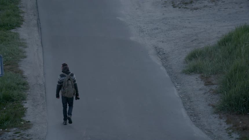 A man is hiking down a road on a cloudy day