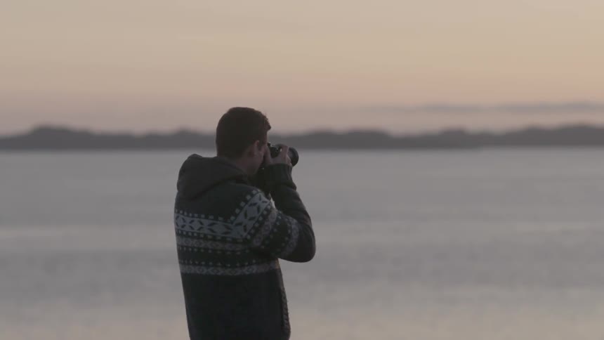 A man stands near a lake at dawn taking pictures