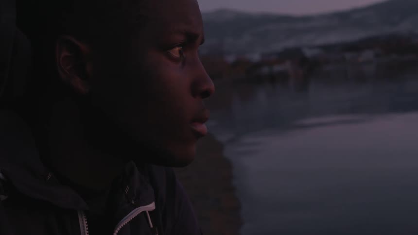 A man sits on the beach looking at the water at sunset