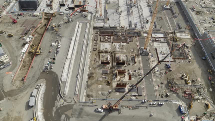 Construction cranes working above a deep underground pit bordered by heavy equipment and various building supplies