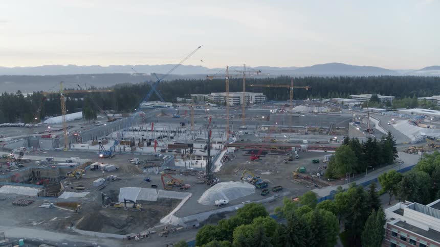 Wide orbit around an enormous construction site filled with cranes, heavy equipment and workers
