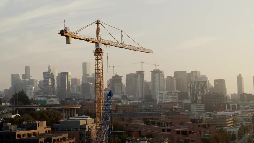 A large construction crane stands tall in front of a metropolitan city skyline