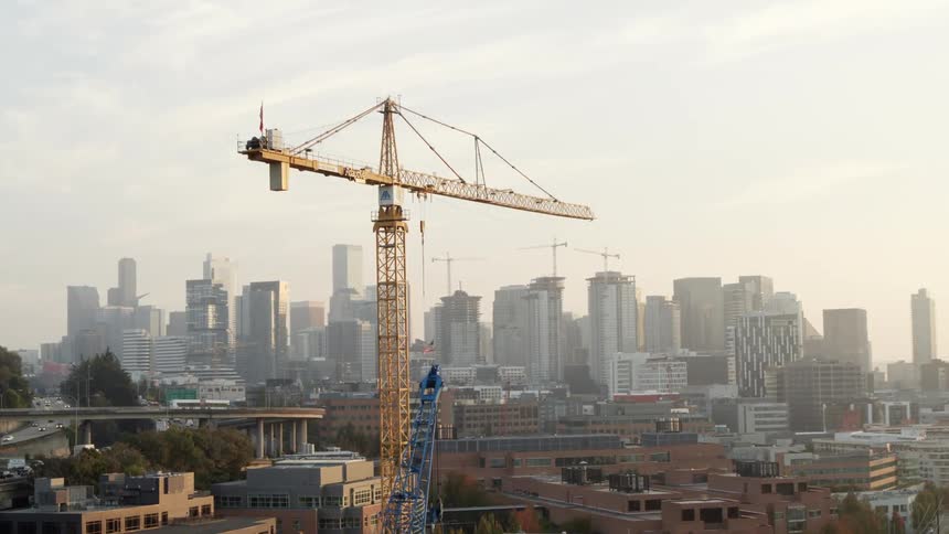 Orbiting around a tall tower crane in front of a city skyline with many buildings under construction in the distance