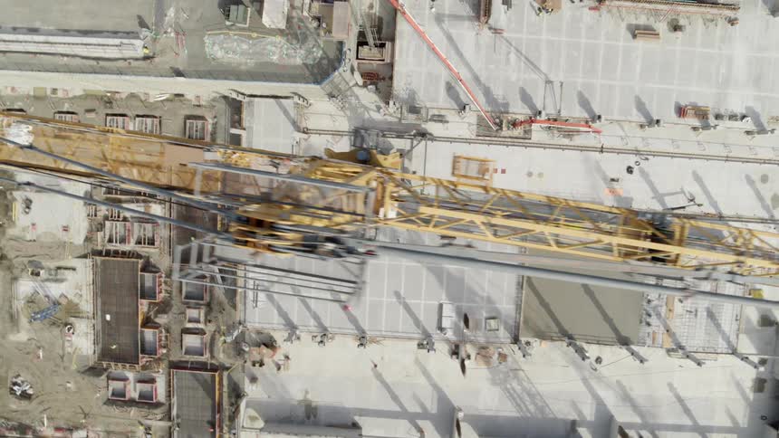 Skimming along the top edge of a tall tower crane working at a construction site