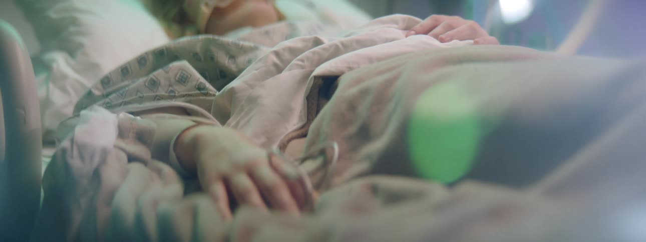 A female patient in a hospital bed remains completely motionless