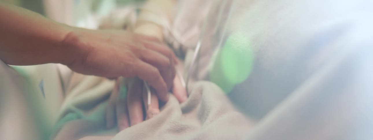 A glare of sunlight over a hand holding a patients hand in a hospital bed