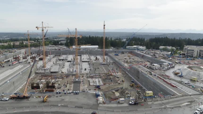 Ascending over an enormous construction site bustling with tall cranes and heavy equipment