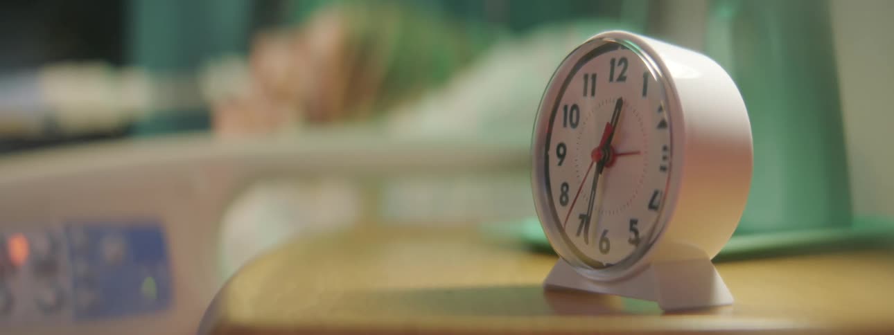 An alarm clock next to a person sleeping