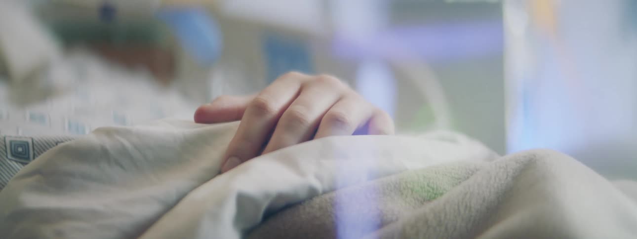 A man lies in a hospital bed and rests his hand on his stomach