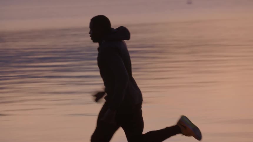 A man is running along a shoreline at sunset