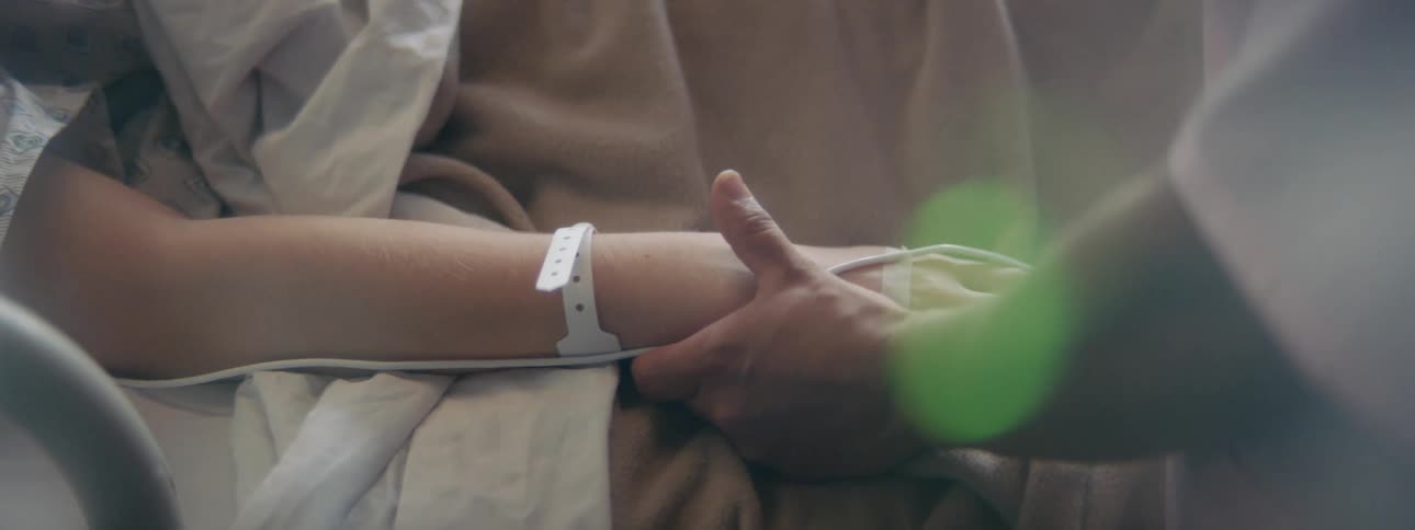 A woman is holding a patients hand in bed
