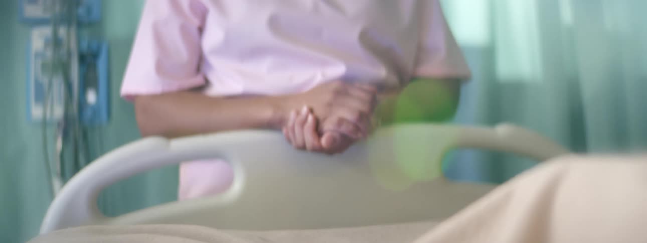 A nurse with scrubs standing at the foot of the hospital bed