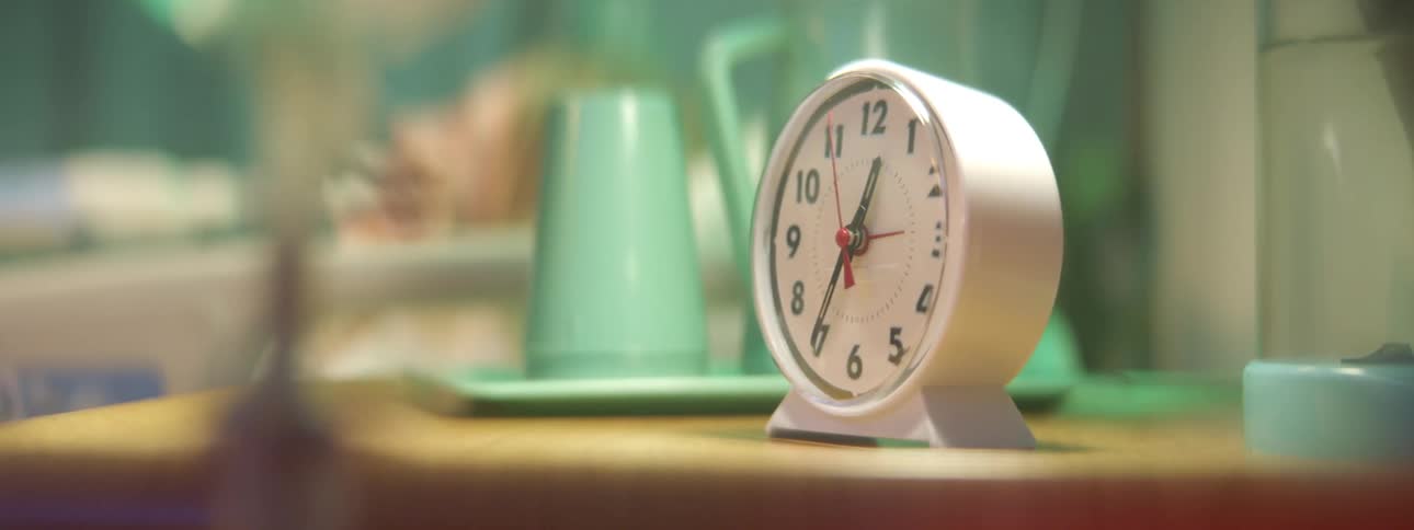 Analog table clock on a table next to the bed of a patient in a hospital room