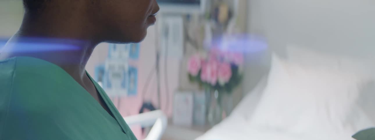 A woman in scrubs stands in a hospital room near an empty bed