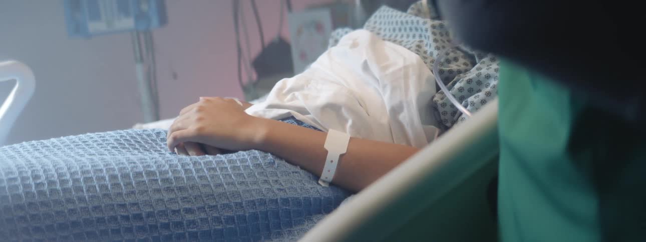 A female patient is laying in a hospital bed as medical staff is working nearby