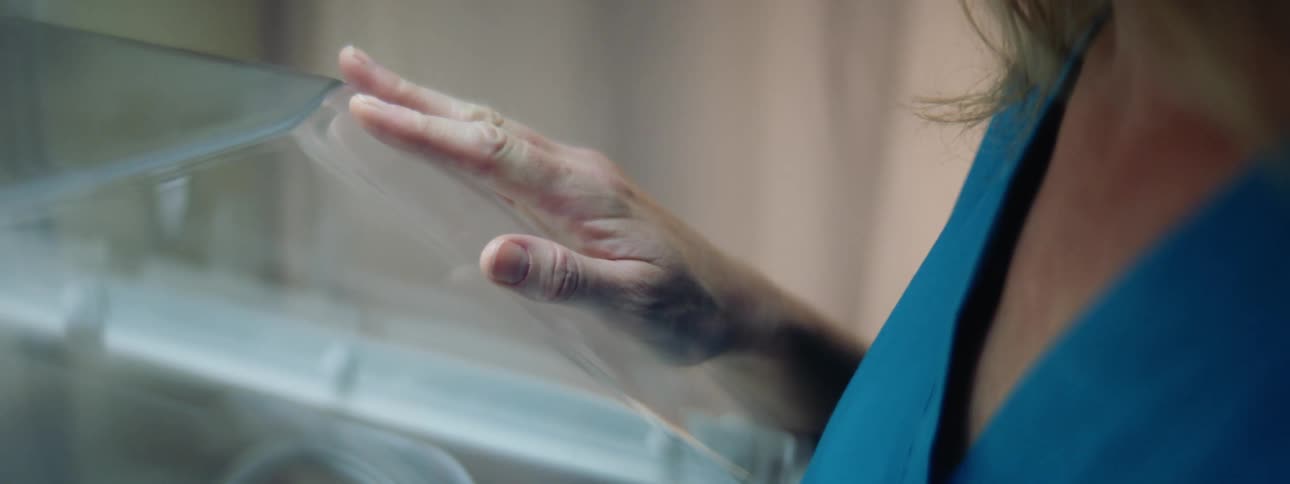 A nurse checks on an infant patient in an incubator in neonatal care