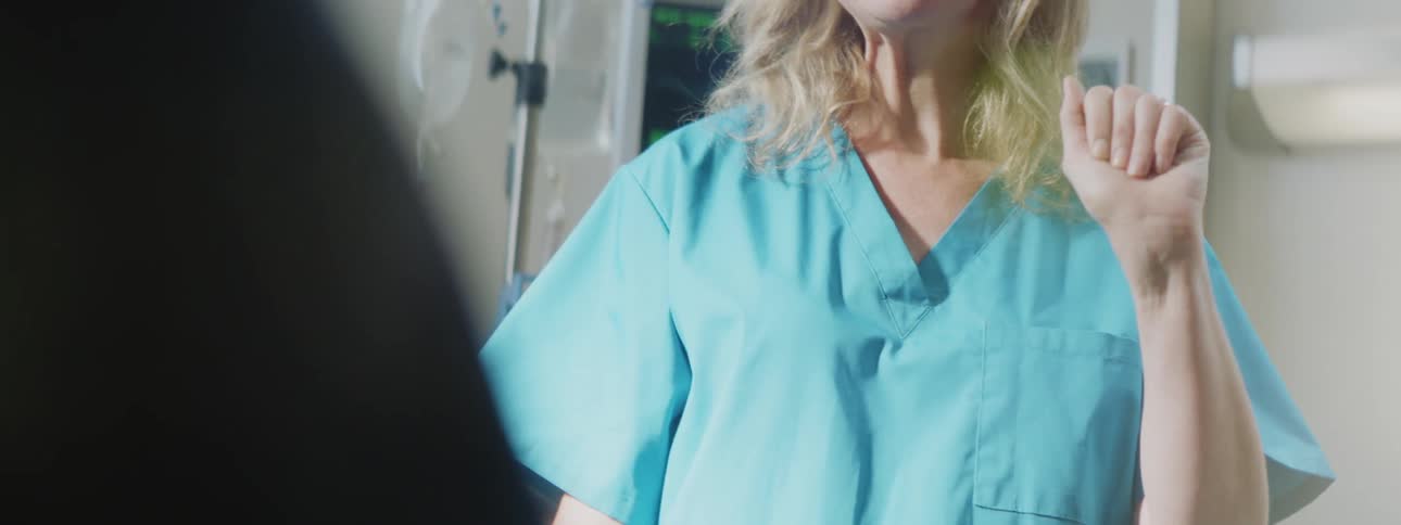 Nurse in blue scrubs waves to a patient inside a hospital room