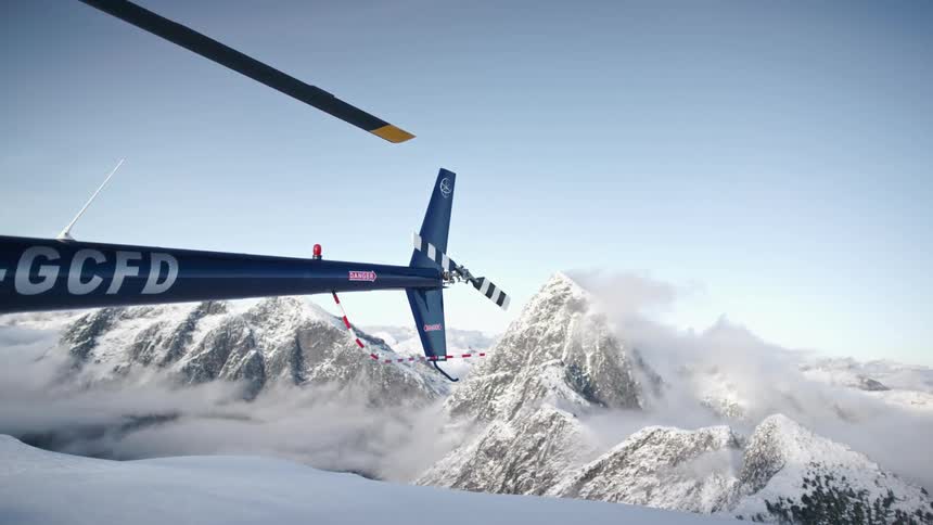 The tail of a blue helicopter against snow and mountains on a clear day