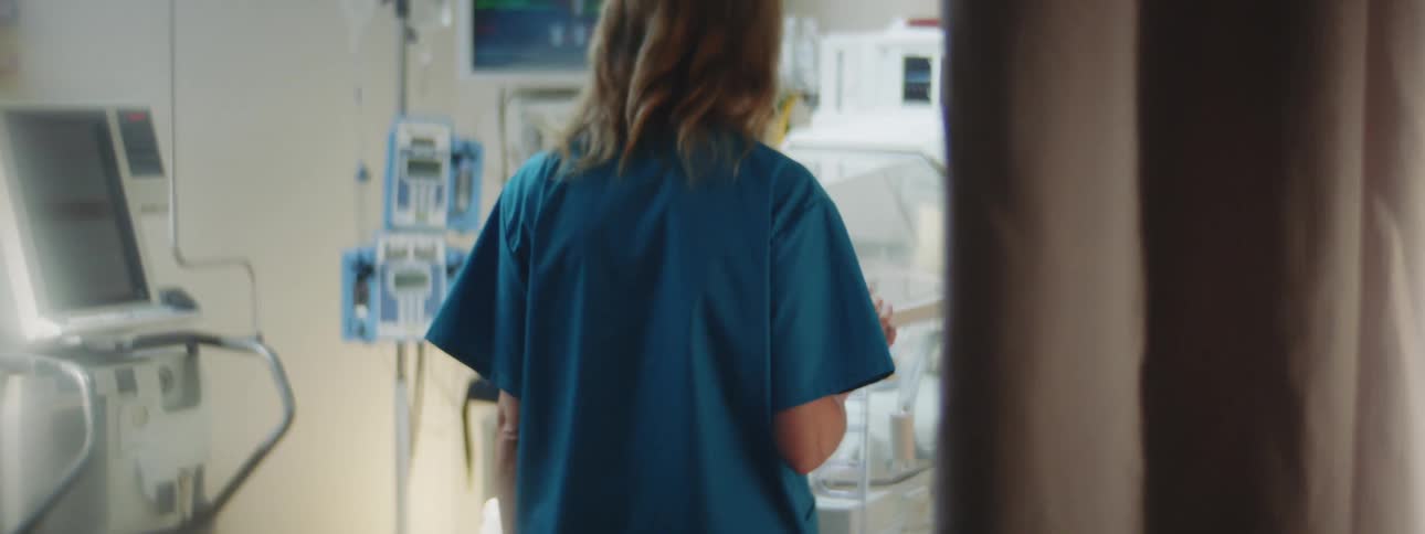 Woman walks into a hospital room and looks at a baby in an incubator