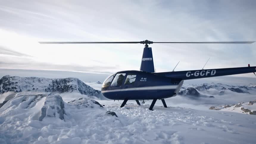 A blue helicopter with propellers moving sits on a snow covered ground during the day