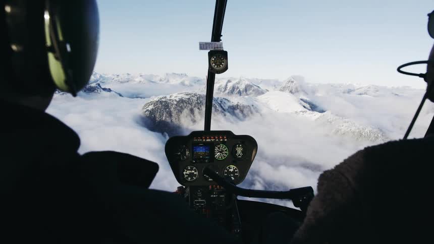 A helicopter pilot flies above clouds at the top of a mountain range