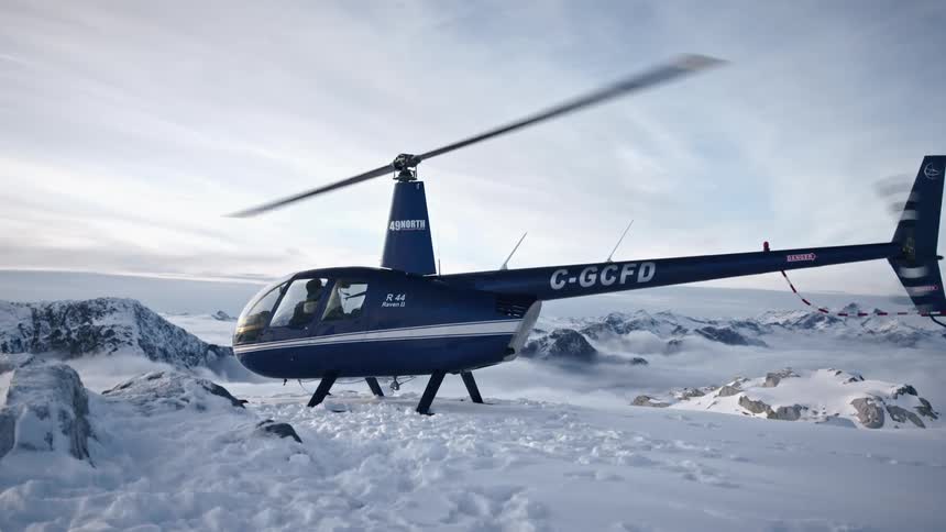 A person sitting in a helicopter stopped on a snow covered mountain