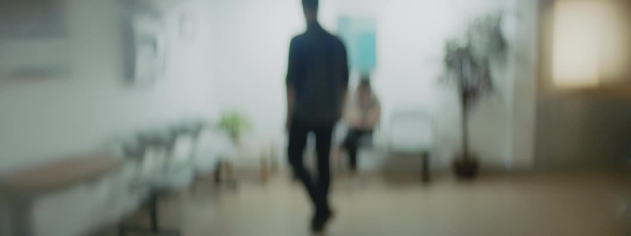 A man pushes a door open and walks in to a waiting room and sits down