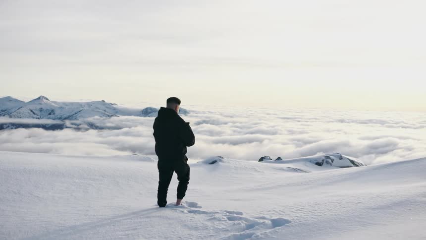 Man taking pictures of the clouds over the snow covered peaks of a mountain range