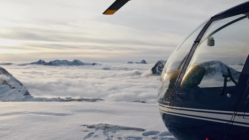 Helicopter parked on top of a snowy mountain next to a cliff overlooking other mountains