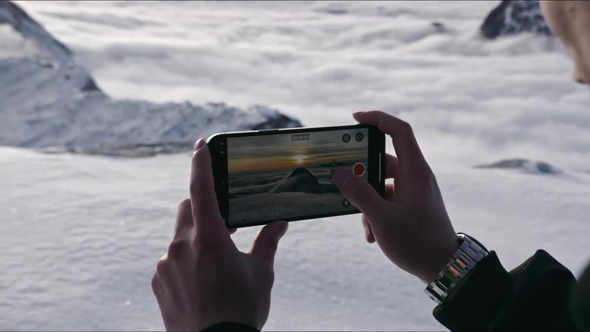 A person holds up their smart phone in order to take a picture of snow capped mountains