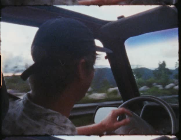 Man driving a car with the sunroof open on a road through the mountains